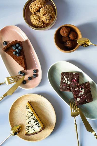 Farklı renklerde tabaklarda çilek ve fındık ile kek tatlılar Dilimleri, pembe, yeşil, ahşap malzeme. Yemek için bıçaklı Altın Çatal. Çay kaşığı. Çikolata, kek, cheesecake, bisküvi.