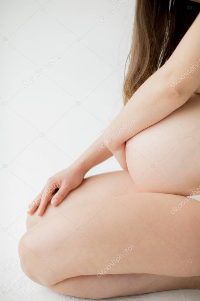 Happy young mother in anticipation of the birth of the baby. A pregnant girl is sitting clasping her bare belly. On a white background.