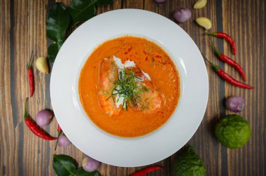 Geleneksel Tayland yemeği karidesi baharatlı köri soslu, sebze malzemesi süslemeli, yakın çekim, ahşap masa arkasına kurulmuş..