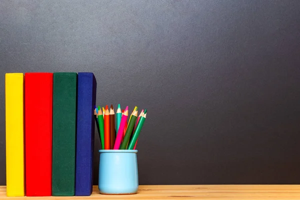 Učebnice a barevné pence v držáku Pensil na pozadí hrací desky. — Stock fotografie