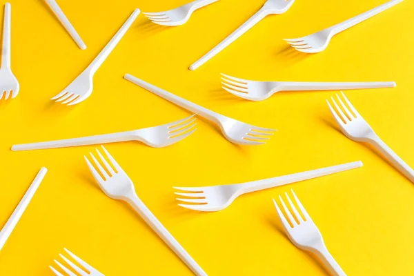 Disposable white plastic forks on yellow background.