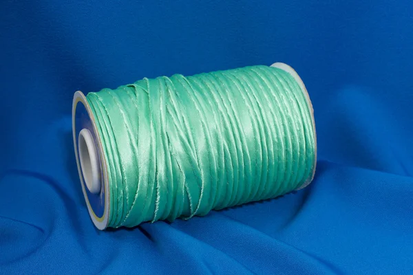 Шелковая зеленая коса для шитья на голубой ткани . — стоковое фото