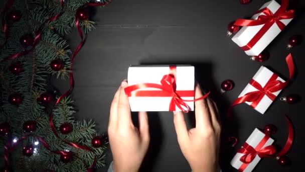 圣诞节背景的黑色木材装饰与冷杉分枝 松树上装饰着红色的五彩纸屑和闪烁的灯光 白色礼物与红色丝带 一个男孩把礼物放在桌子上 然后拿回来 顶部视图 用于问候语消息的空间 — 图库视频影像
