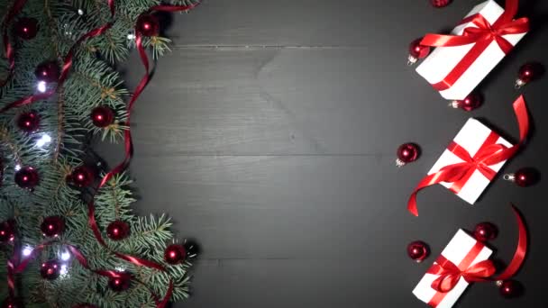 圣诞节背景的黑色木材装饰与冷杉分枝 松树上装饰着红色的五彩纸屑和闪烁的灯光 白色礼物与红色丝带 一个男孩把礼物放在桌子上 顶部视图 用于问候语消息的空间 以4K 分辨率拍摄 — 图库视频影像