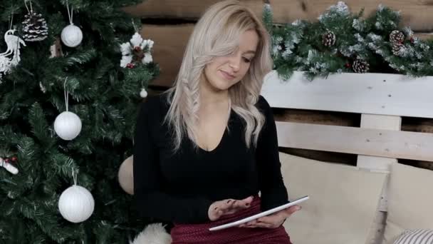 一个女仆在圣诞节的气氛中 在网上和她的平板电脑上交流和聊天 用白色玩具装饰的松树 — 图库视频影像