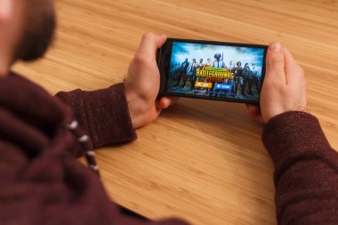 Prague, Çek Cumhuriyeti - 16 Mart 2019: bir akıllı telefon ve kelepçelememz Playerunknown s Battlegrounds mobil oyun tutan adam. Bir bambu zemin üzerine açıklayıcı bir editoryal görüntü.