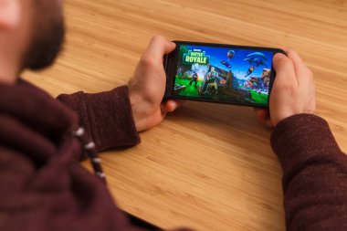 Prague, Çek Cumhuriyeti - 16 Mart 2019: bir akıllı telefon ve kelepçelememz Fortnite tutan adam: Battle Royale mobil oyun. Bir bambu zemin üzerine açıklayıcı bir editoryal görüntü.