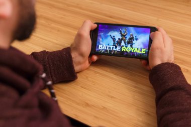 Prague, Çek Cumhuriyeti - 16 Mart 2019: bir akıllı telefon ve kelepçelememz Fortnite tutan adam: Battle Royale mobil oyun. Bir bambu zemin üzerine açıklayıcı bir editoryal görüntü.