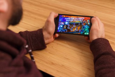 Prague, Çek Cumhuriyeti - 16 Mart 2019: bir akıllı telefon ve kelepçelememz Marvel Yarışması Şampiyonu mobil oyun tutan adam. Bir bambu zemin üzerine açıklayıcı bir editoryal görüntü.
