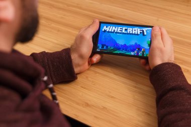 Prague, Çek Cumhuriyeti - 16 Mart 2019: Minecraft mobil oyun tutan bir smartphone ve kelepçelememz adam. Bir bambu zemin üzerine açıklayıcı bir editoryal görüntü.