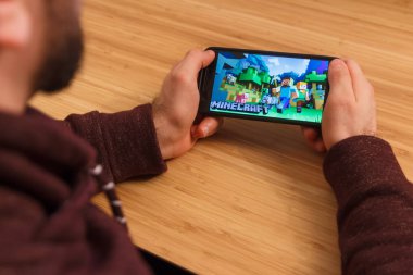 Prague, Çek Cumhuriyeti - 16 Mart 2019: Minecraft mobil oyun tutan bir smartphone ve kelepçelememz adam. Bir bambu zemin üzerine açıklayıcı bir editoryal görüntü.