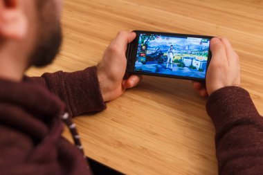 Prague, Çek Cumhuriyeti - 16 Mart 2019: bir akıllı telefon ve kelepçelememz hayatta kalma kuralları mobil oyun tutan adam. Bir bambu zemin üzerine açıklayıcı bir editoryal görüntü.