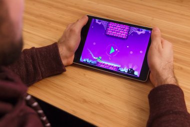 Prague, Çek Cumhuriyeti - 16 Mart 2019: bir akıllı telefon ve kelepçelememz geometri Dash mobil oyun tutan adam. Bir bambu zemin üzerine açıklayıcı bir editoryal görüntü.