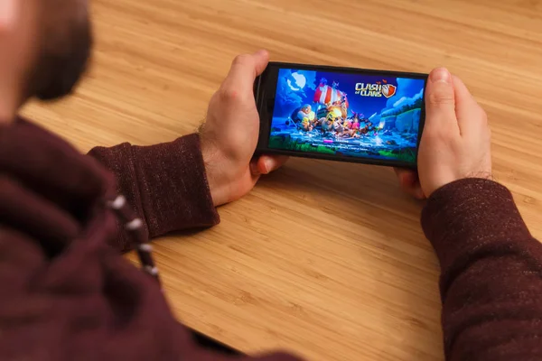 Prag, Tjeckien - 16 mars 2019: Man håller en smartphone och SPLA Clash of Clans mobila spelet. En belysande redaktionell bild på en bambu bakgrund. — Stockfoto