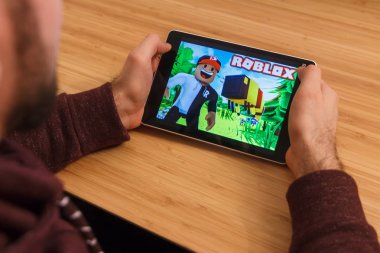 Prague, Çek Cumhuriyeti - 16 Mart 2019: bir akıllı telefon ve kelepçelememz Roblox mobil oyun tutan adam. Bir bambu zemin üzerine açıklayıcı bir editoryal görüntü.