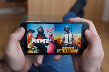 LOS ANGELES, CALIFORNIA - JUNE 3, 2019: Lying Man holding a smartphone and compares PUBG and Fortnite games on the smartphone screen. An illustrative editorial image. clipart