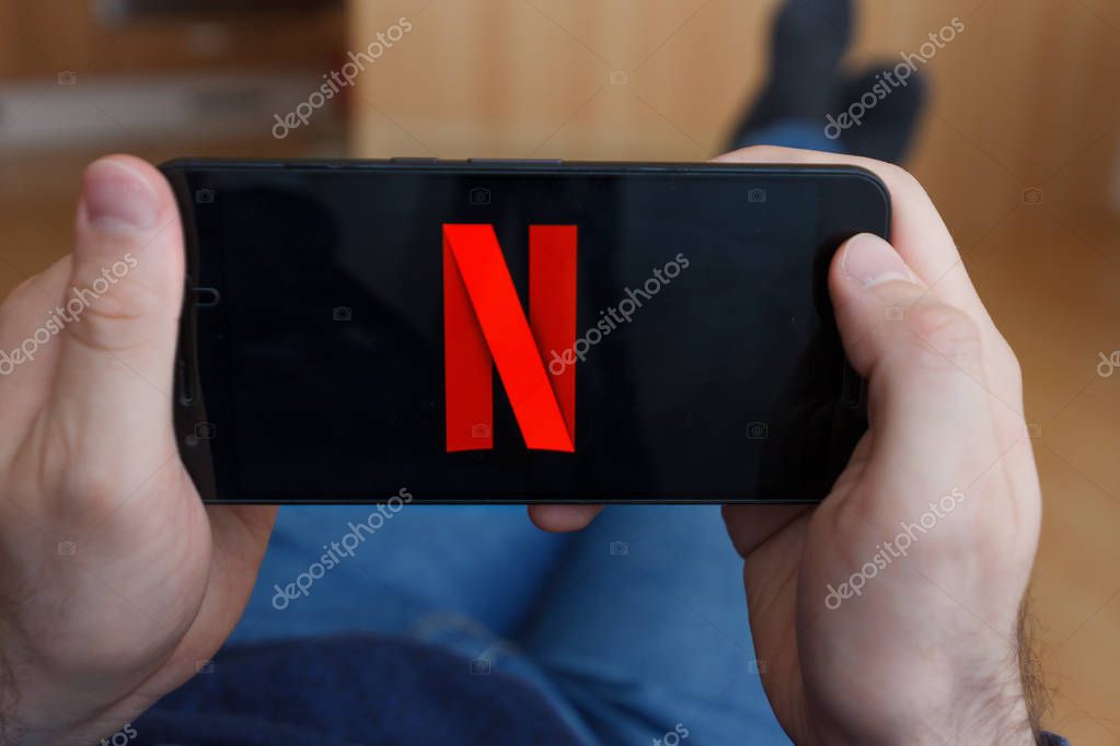 LOS ANGELES, CALIFORNIA - JUNE 3, 2019: Close up to male hands holding smartphone watching Netflix. An illustrative editorial image.