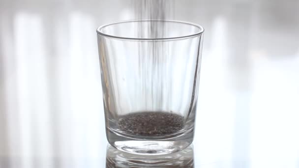 Les graines de chia se déversent dans un verre vide transparent. Verser les gruaux dans un verre transparent . — Video