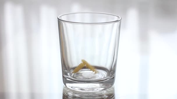 Pasta Torchietto is Pouring into a Transparent Empty Glass. Pouring groats into a clear glass — Stock Video