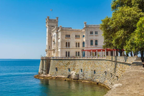 Miramare castle building above Adriatic sea. The view of beautiful Miramare castle located close to the sea. Three colour sea water and a castle on the seaside. A clean transparent water of Adriatic s