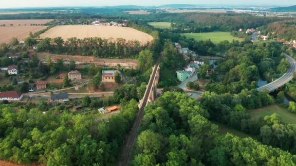 Luftaufnahme des alten Brückenviadukts im grünen Wald in der Nähe des Dorfes. Eisenbahn über Tal. — Stockvideo