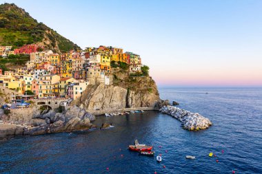 Cinque Terre, La Spezia 'daki Manarola Panoraması. Ligurian Denizi yakınlarındaki renkli binalar. Gün batımında mavi suyla marinada demirlemiş teknelerin manzarası.
