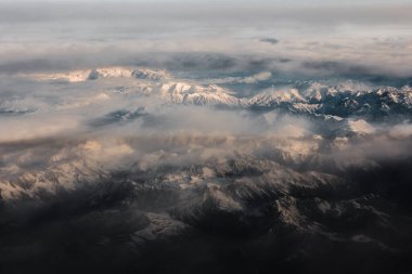 Alp Dağları ve Tepeleri 'nin panoramasındaki uçaktan hava görüntüsü. Bulutlar ve sis ile kaplı kayalardan oluşan dağ zirvesi. Dağ manzarası yukarıdan görünüyor.