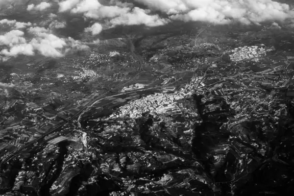 Aerial view from the plane on the panorama of the city through the clouds. View from above on the town near the mountains and hills ridge. View from above on mountain landscape.