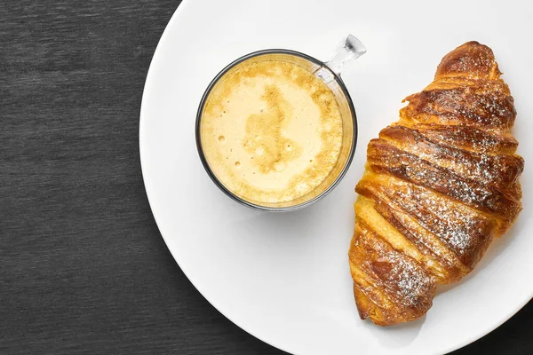 Vista superior de cappuccino e croissant em uma placa em um fundo preto com espaço de cópia. Conceito de um saboroso café da manhã. Pastelaria francesa ou italiana . — Fotografia de Stock