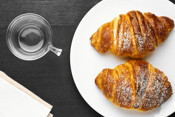 Draufsicht auf Croissants mit Zuckerpuder und einer leeren Tasse auf schwarzem Hintergrund — Stockfoto