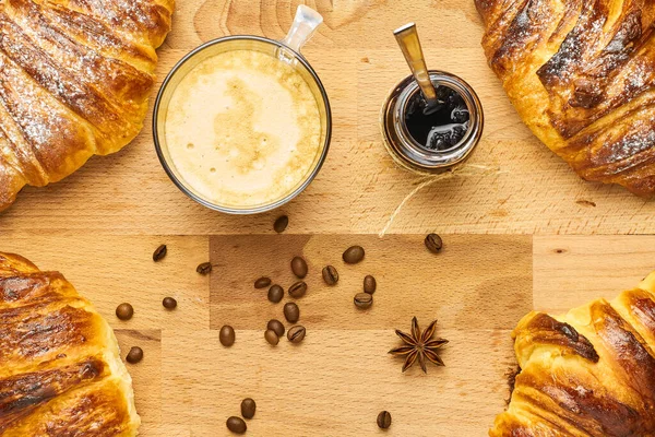 Posa piatta di croissant in angoli, caffè, vaso di marmellata e chicchi di caffè con anice stellato nel mezzo. Concetto colazione . — Foto Stock