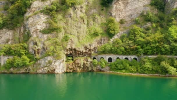 Vlucht langs tunnel Grumo in een rots naast het Comomeer met groen water, Italië. Tunnel bedekt met groene bomen. — Stockvideo