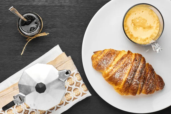 Vue de dessus sur un petit déjeuner français servi avec cappuccino, moka, croissant et confiture sur fond noir . — Photo