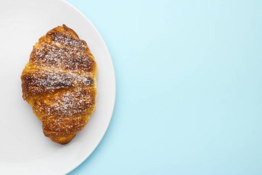 Kahverengi kabuklu şeker tozlu lezzetli kruvasan mavi arka planda fotokopi alanı var. Kafe reklamı kavramı.