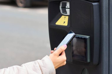 Akıllı telefonuyla park ücretini ödeyen genç bir kadın. Kopya alanı ile temassız ödeme yolu.