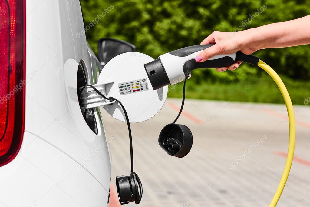 Woman unplugging a charger from an electric car socket. Eco friendly vehicle with zero emission