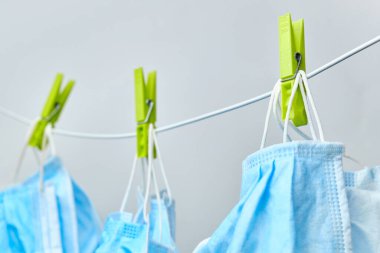 Çamaşır ipinde mavi koruyucu maske ve beyaz arka planda yeşil mandallarla kurutuluyor. Koronavirüsün önlenmesi yayılıyor.