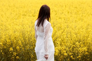 Sarı kolza tohumu tarlasında dikilen beyaz elbiseli kadın. Bahar konsepti