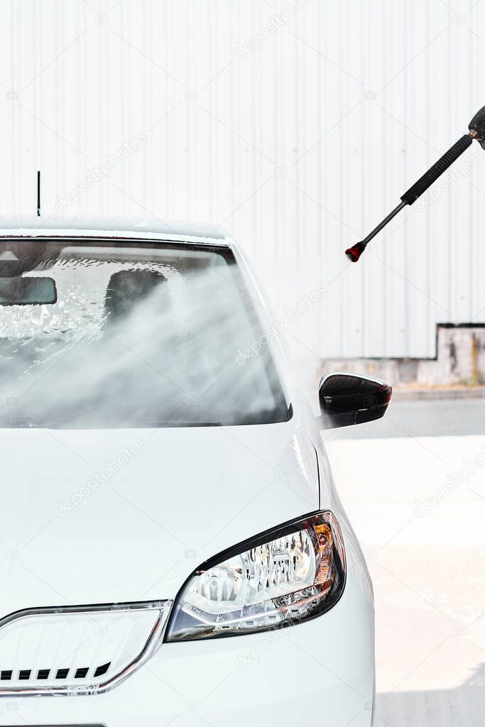 A white car washing with pressurized water at self wash service outdoors at sunny day. Manual car wash concept