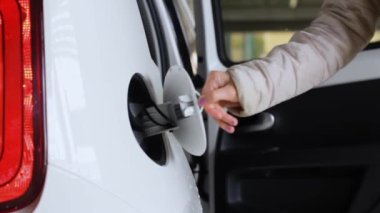 Kadın elektrikli beyaz bir arabanın şarj prizini bağlıyor. Çevre dostu ve sıfır emisyonlu araba.