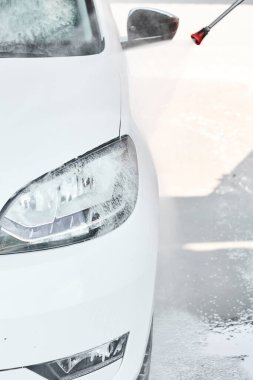 Yüksek basınçlı araba yıkama sırasında su jetinin altındaki beyaz bir arabanın farına yakın çekim.