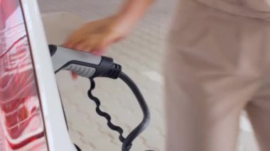 EV bataryasını şarj etmek için elektrik kablosunu elektrikli arabaya bağlayan kadın.. 