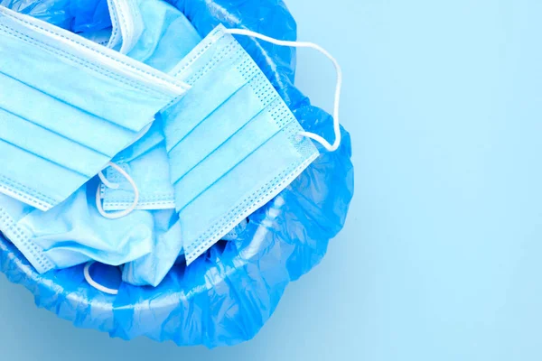 Disposable surgical mask is thrown to the trash bin on a blue background with copy space. Coronavirus and quarantine is over. End of pandemic