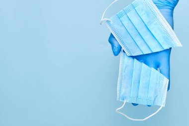 Mavi arka planda kesilmiş yüz maskesi tutan koruyucu eldivenler ve fotokopi alanı olan koruyucu eldivenler veriyorlar. Coronavirus, SARS-CoV-2 salgını sona erdi. Karantinanın sonu. 