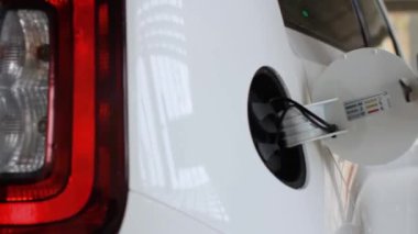 Kadın, halka açık alanda araba şarj etmek için elektrikli araba EV 'si takıyor.