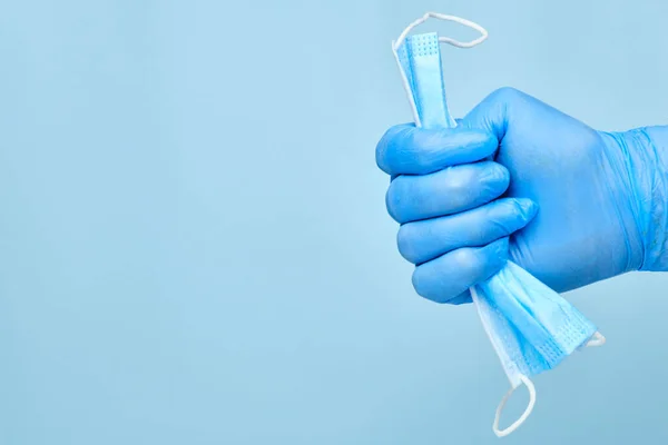 Uomo mano in gomma guanti blu tenuta utilizzato maschera protettiva usa e getta su uno sfondo blu con spazio copia. Coronavirus, la SARS-COV-2 e 'finita. Fine della pandemia e della quarantena. Spazzatura medica. — Foto Stock