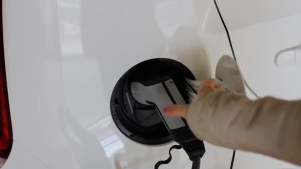 O femeie scoate o priză din priza maşinii de la staţia publică de încărcare. Finisarea reîncărcării bateriei vehiculului electric . — Videoclip de stoc