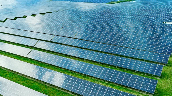 Central solar en el campo verde. El cielo azul y las nubes se reflejan en el panel fotovoltaico. Producción de energía solar . — Foto de Stock