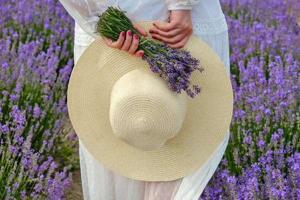 帽子を背にした白い光のドレスを着た若い女性と花に提出された紫色のラベンダーの花束. — ストック写真