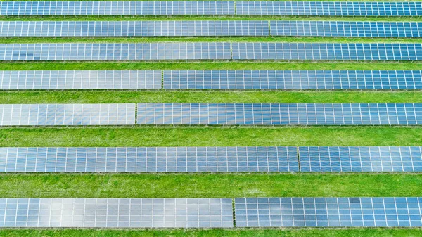 Gleiche Linien von Sonnenkollektoren auf der grünen Wiese. Sonnenkraftwerk zur Erzeugung grüner Energie von oben — Stockfoto